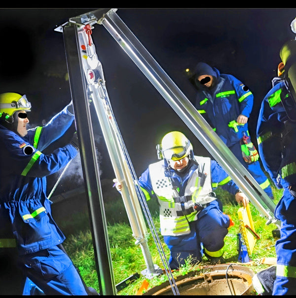 THW-Einsatzkräfte bauen Bautri Rescue nachts als Rettungsdreibein über einem Schacht auf
